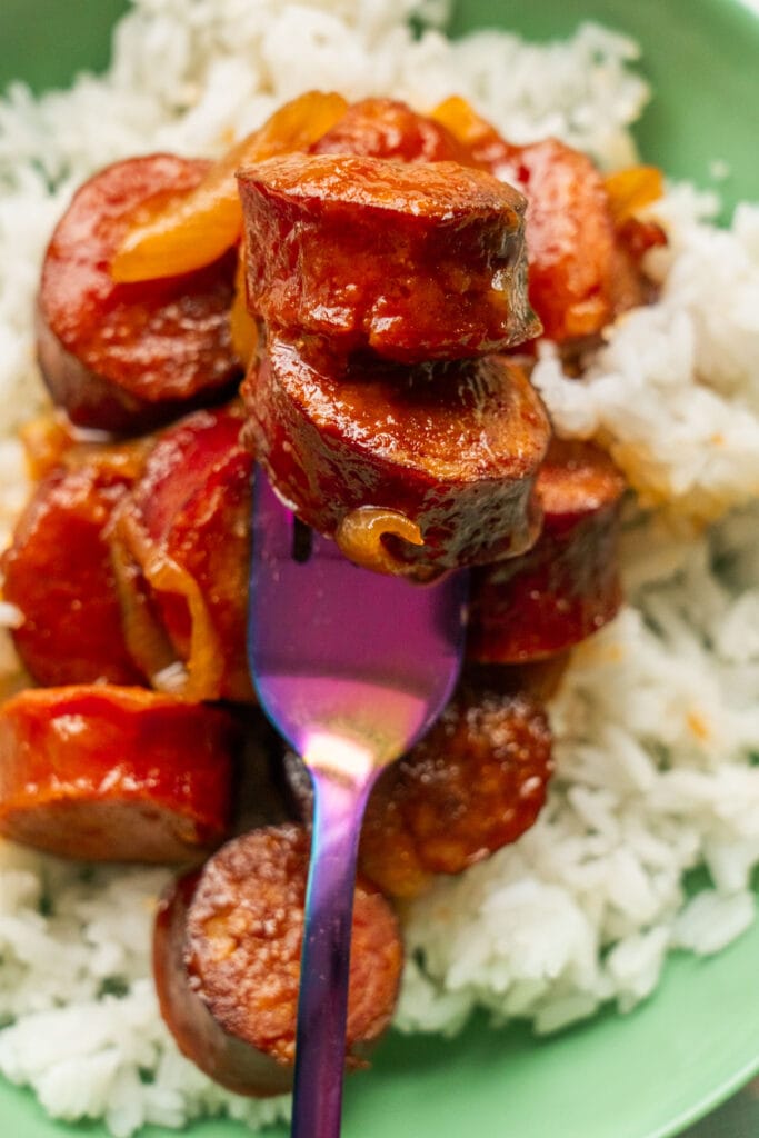 fork with kielbasa on it over rice in green bowl. 