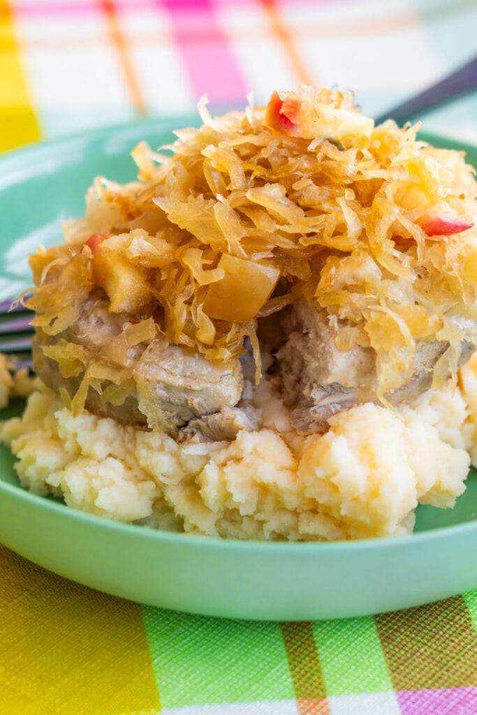 pork chops and sauerkraut over mashed potatoes in green bowl. 