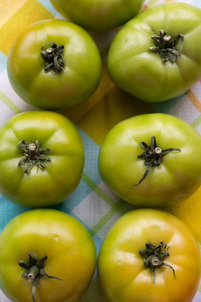 six green tomatoes on table.