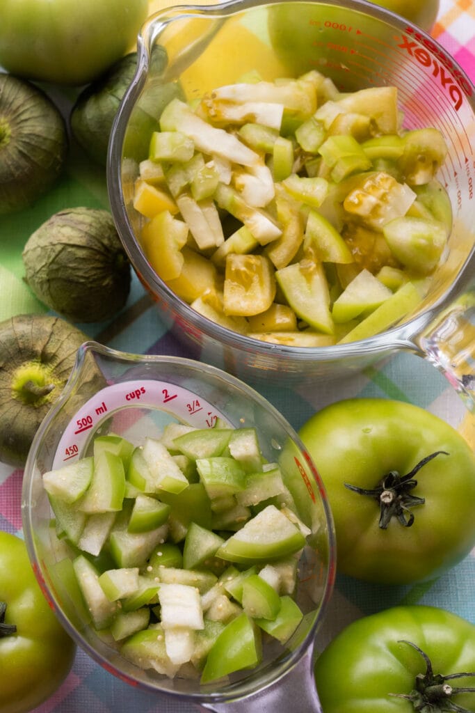 chopped green tomatoes and tomatillos in glass jars on table.