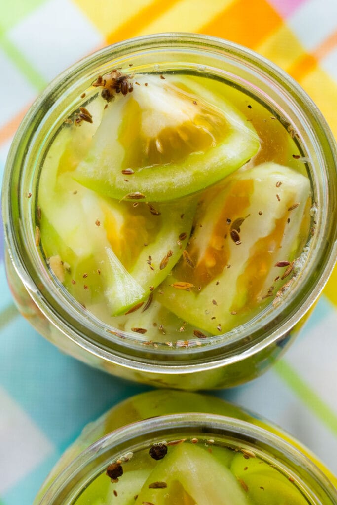 pickled green tomatoes with spices in mason jar.
