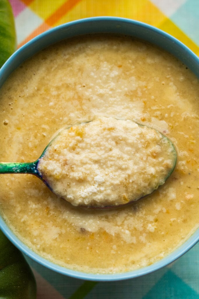 spoon in a bowl of green tomato soup with parmesan cheese melted on top.
