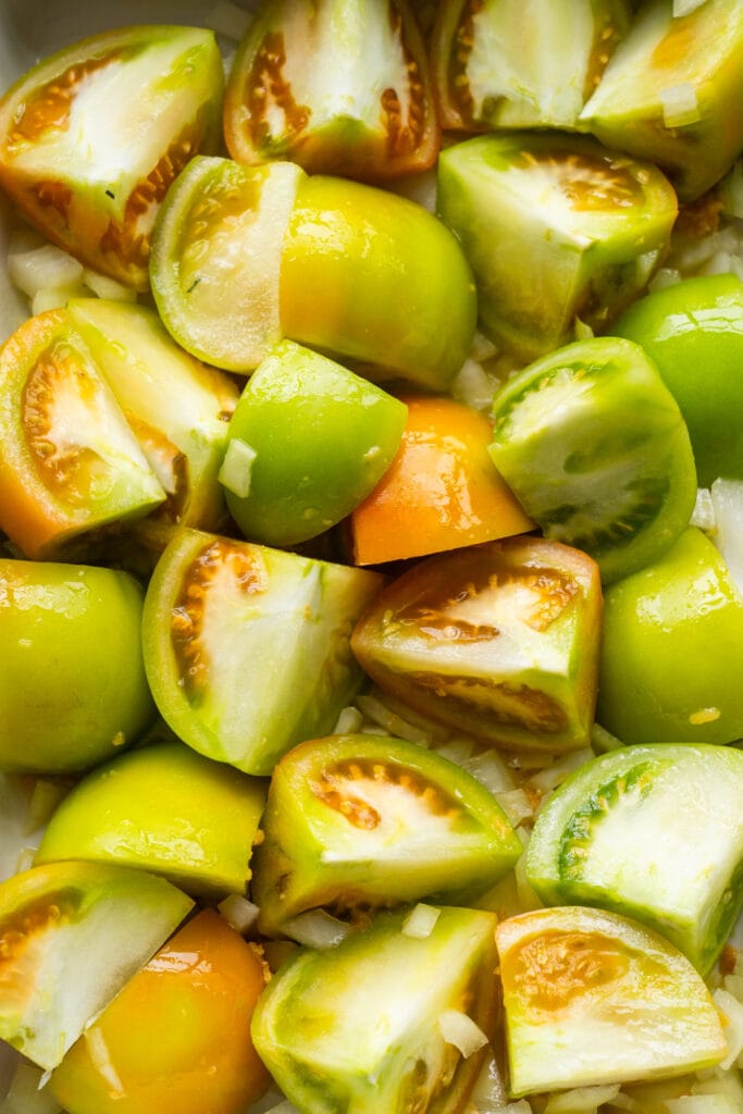 green tomatoes mixed with olive oil in baking dish.