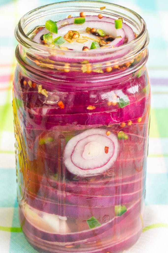 side view of mason jar filled with pickled onions with green specks of jalapeno pepper.