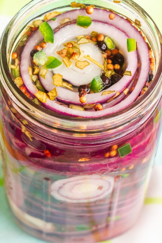 closeup shot of pickled red onions and jalapeno pepper in mason jar.