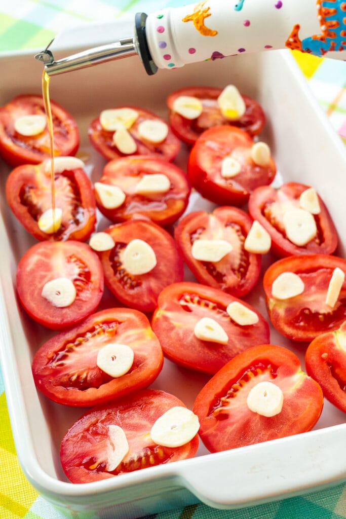 olive oil and minced garlic on top of tomatoes in baking dish.
