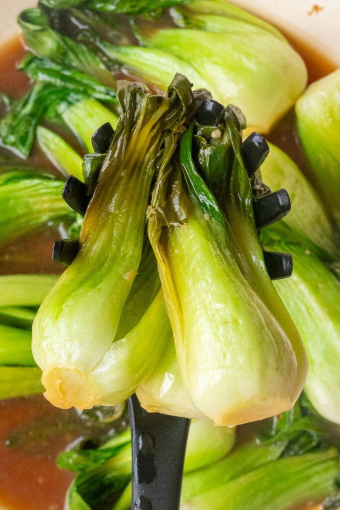 slotted spoon lifting out bok choy from skillet. 