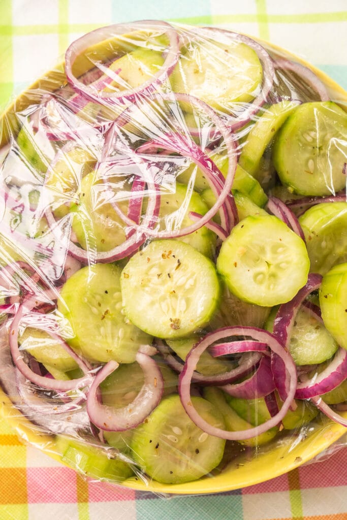 cucumbers and red onions with plastic wrap covering it.