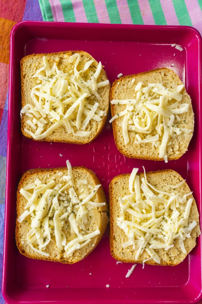 pieces of bread on baking pan with shredded cheese on them.