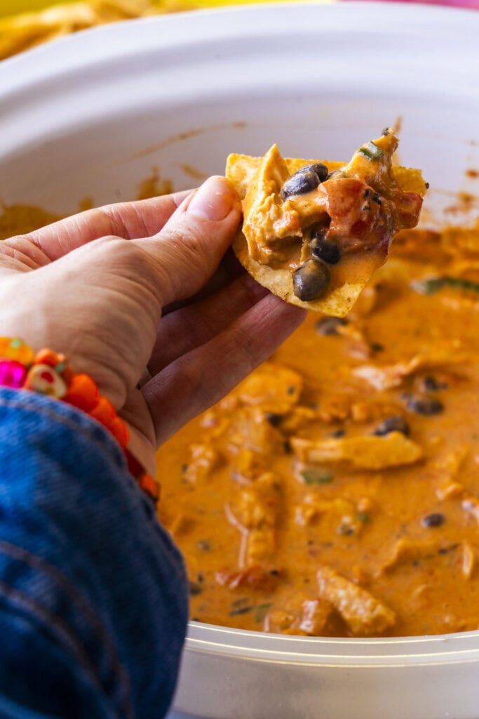hand holding tortilla chip scooping cheese dip out.