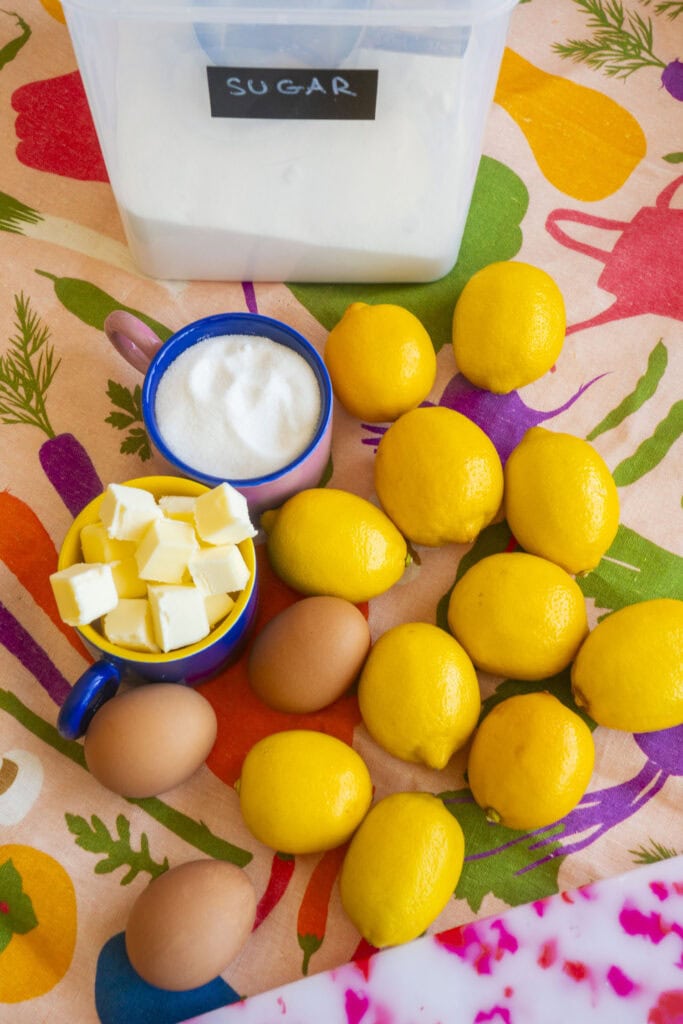 lemons, eggs, sugar and butter on vegetable pattern table cloth.