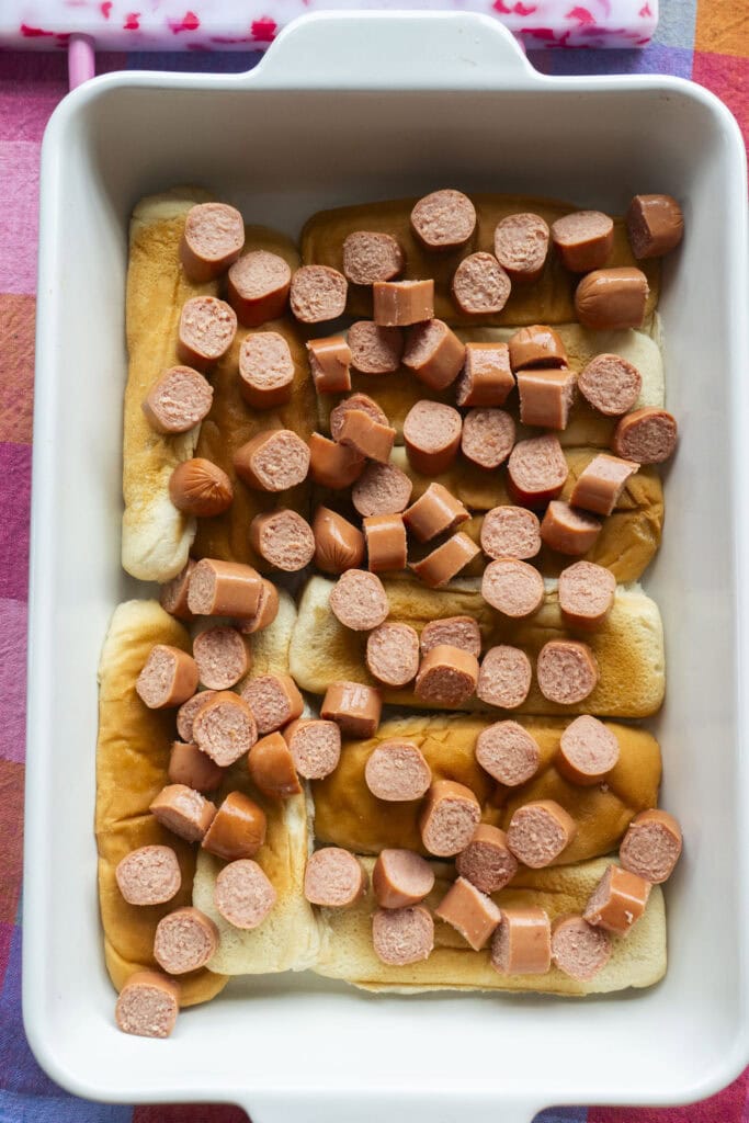 sliced hot dogs on top of buns in casserole dish.