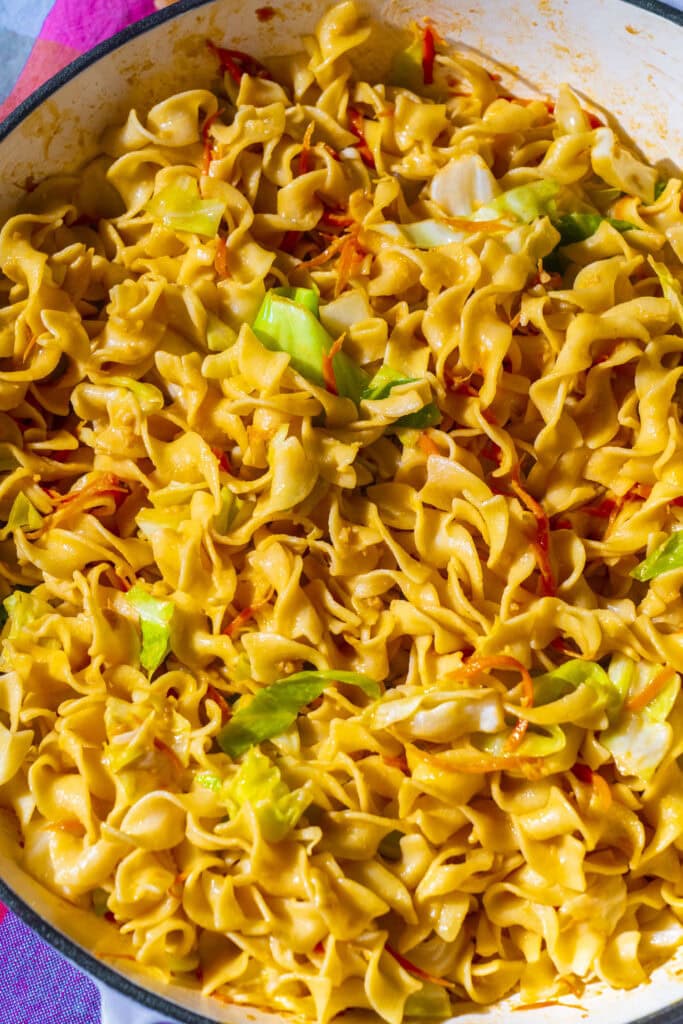 cooked egg noodles with sauted cabbage and carrots in skillet.