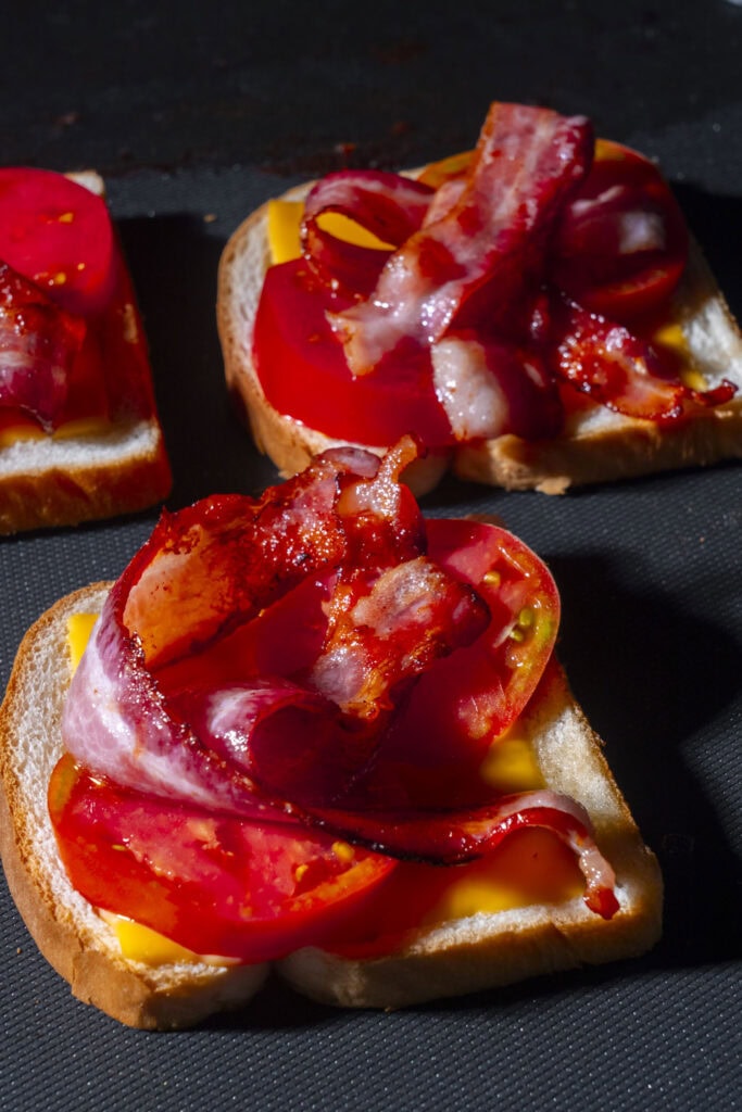 bacon, tomato and cheese on bread on griddle.
