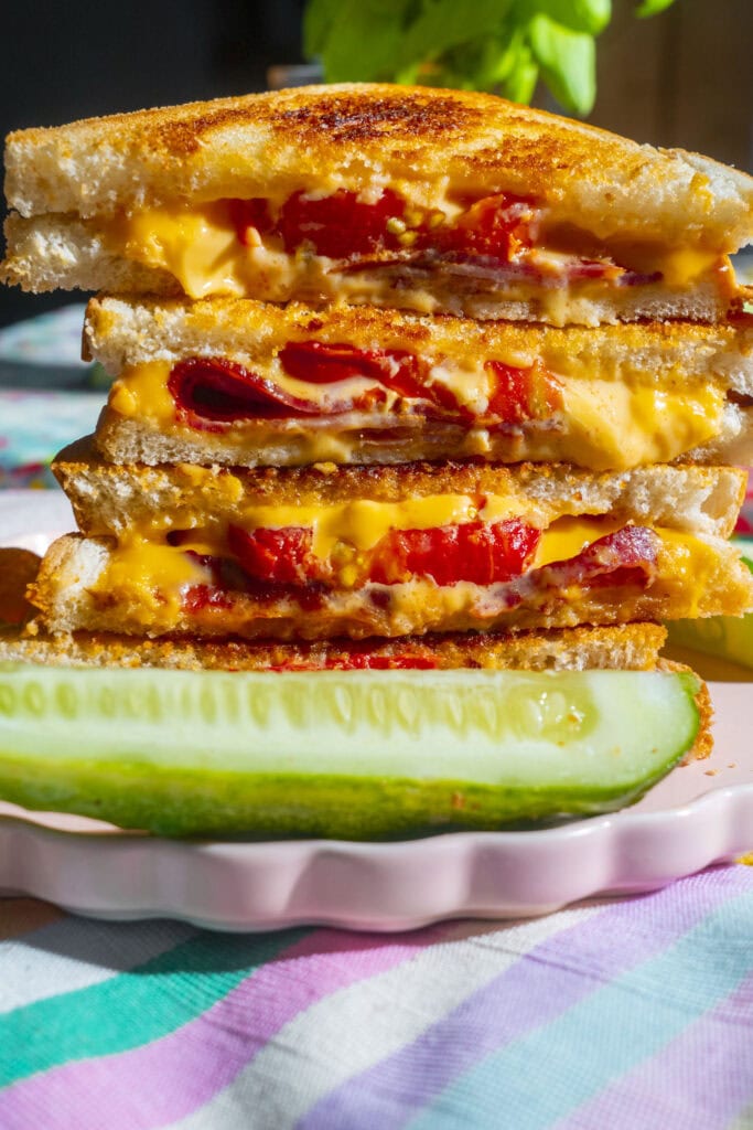 vertical picture closeup of grilled cheese sandwich tomatoes and bacon, sitting next to pickle on plate