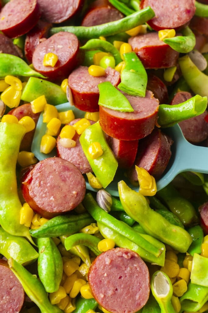 stirred buttery kielbasa, green beans and corn with blue spoon serving it.
