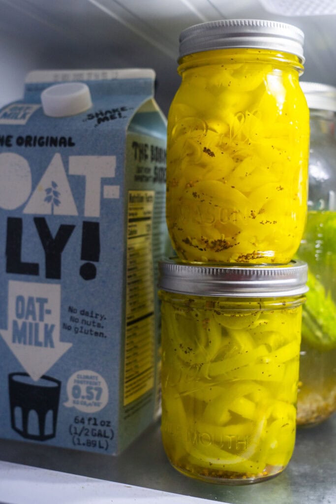 jars of banana peppers nexxt to oat milk in the fridge.
