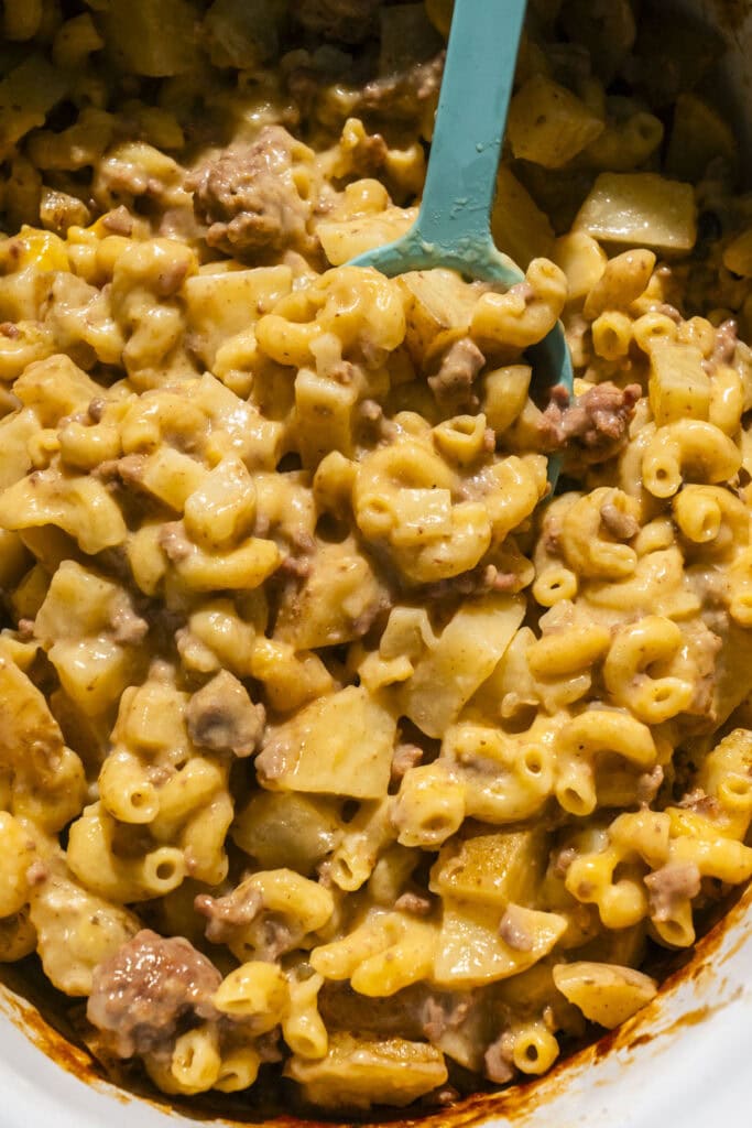 hamburger helper cooked in crockpot with teal spoon going into it.