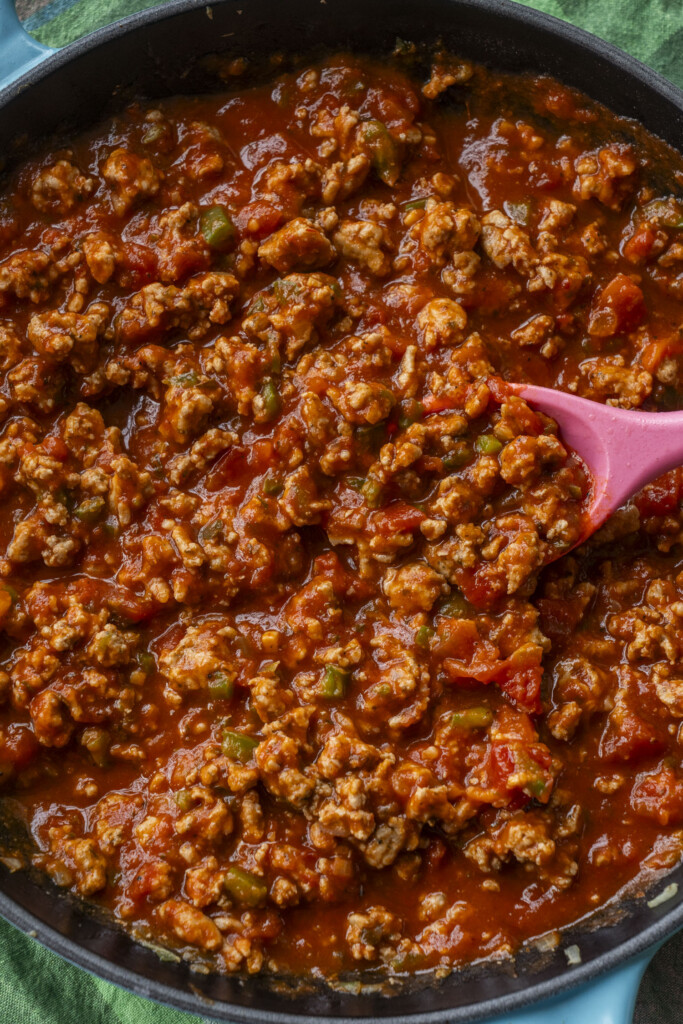 Ground turkey simmering in marinara sauce in a skillet, being stirred with a pink spoon.