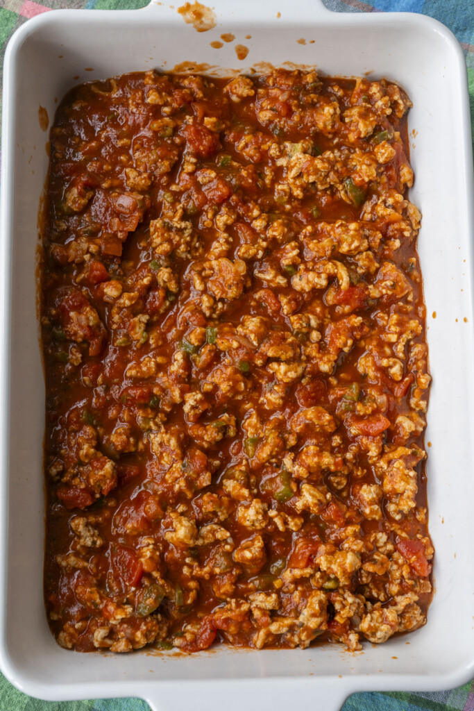 A layer of savory ground turkey and marinara sauce mixture spread into the bottom of a white 9x13 baking dish.