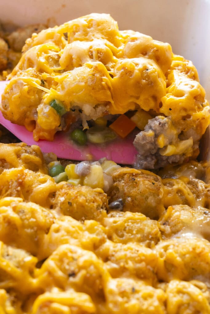 pink spatula scooping casserole out of baking dish.