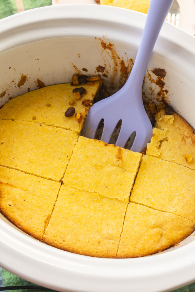 Baked cornbread topping in a white slow cooker cut into even squares.