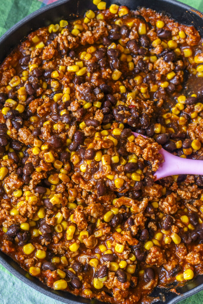 Black beans and corn mixed into the ground turkey enchilada filling in a skillet.