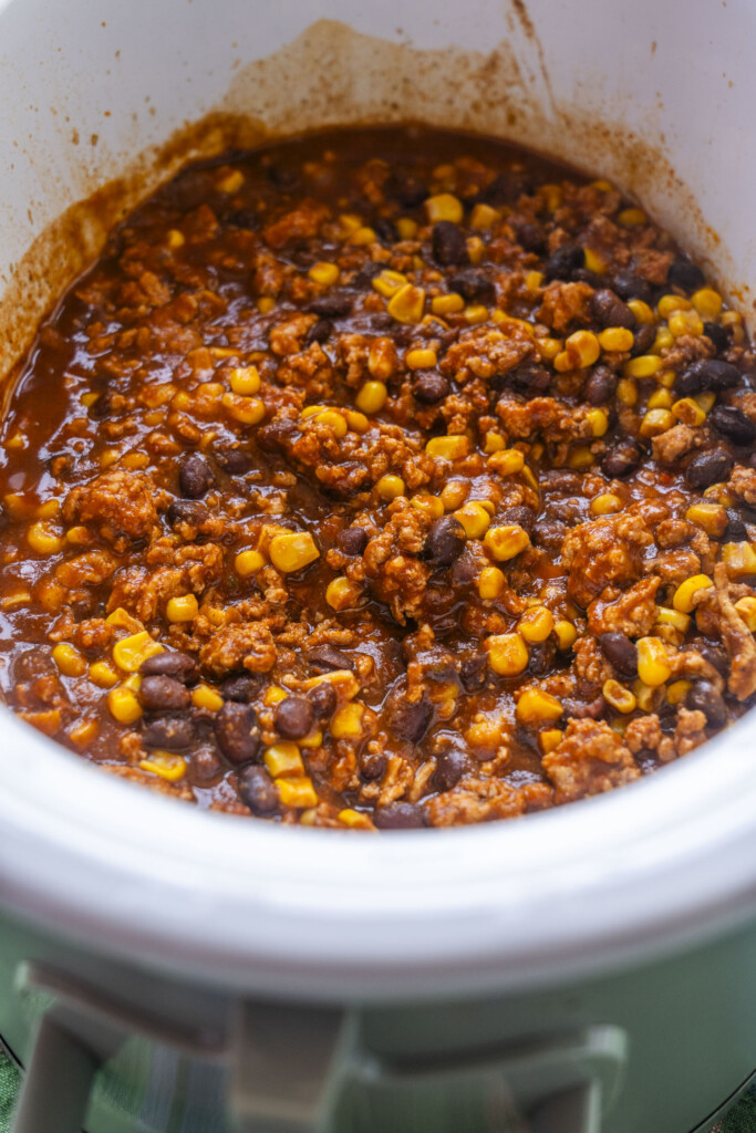 Savory ground turkey and bean filling spread into the bottom of a white slow cooker.