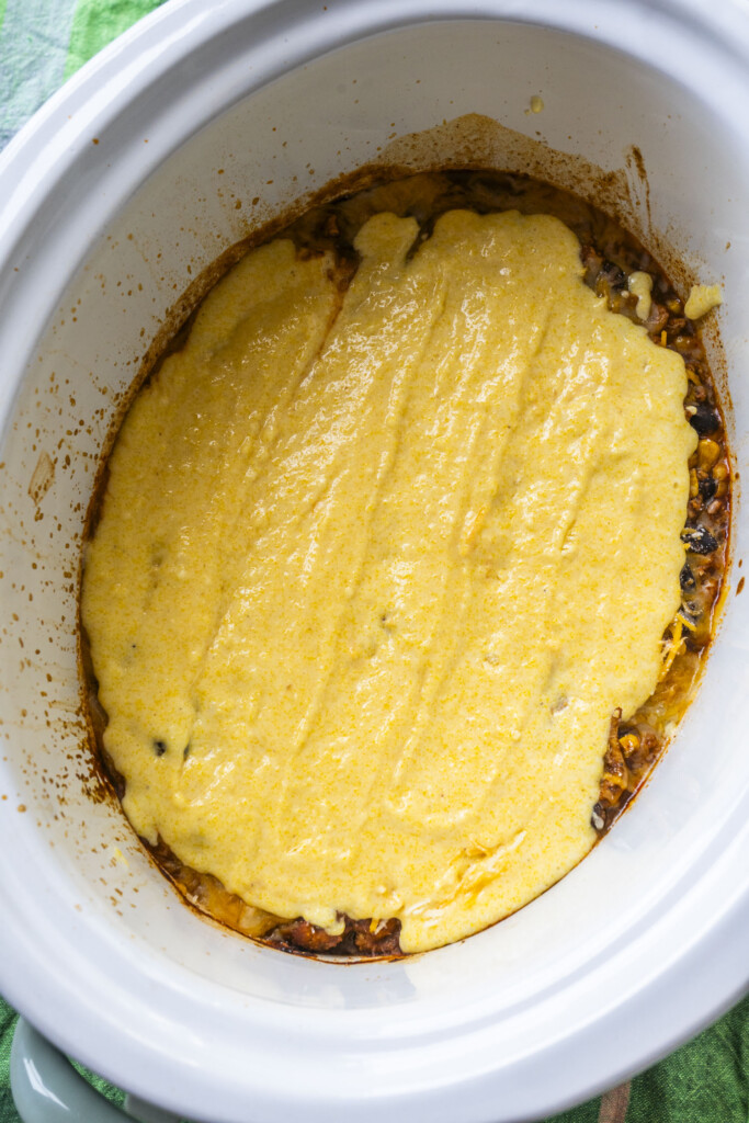 Cornbread batter spread over the cheese layer in the slow cooker