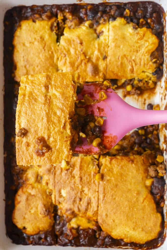 pink spatula lifting out casserole from baking dish.