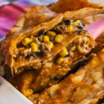 Close-up of a cheesy, layered casserole being served, filled with ground beef, black beans, corn, and melted cheese, with a golden-brown crust on top.