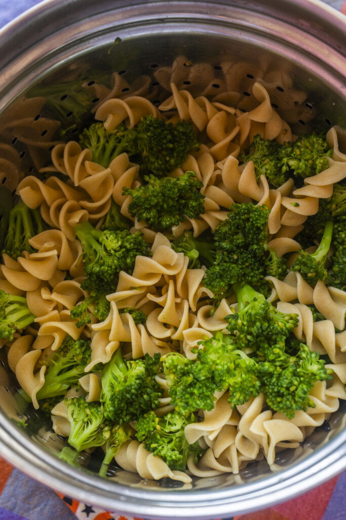 A metal colander filled with cooked rotini pasta and broccoli florets, drained and ready to be served.