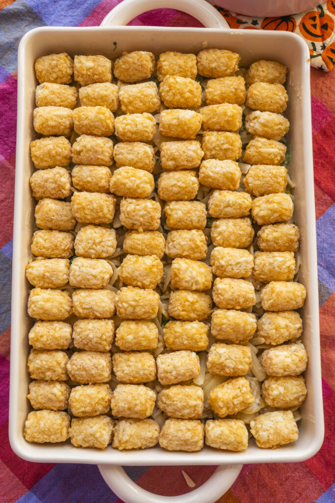 A casserole dish filled with neatly arranged rows of frozen tater tots, placed on top of a colorful, checkered tablecloth.