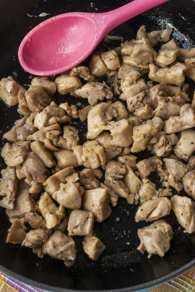 Cooked bite-sized chicken pieces in a skillet with a pink spoon.