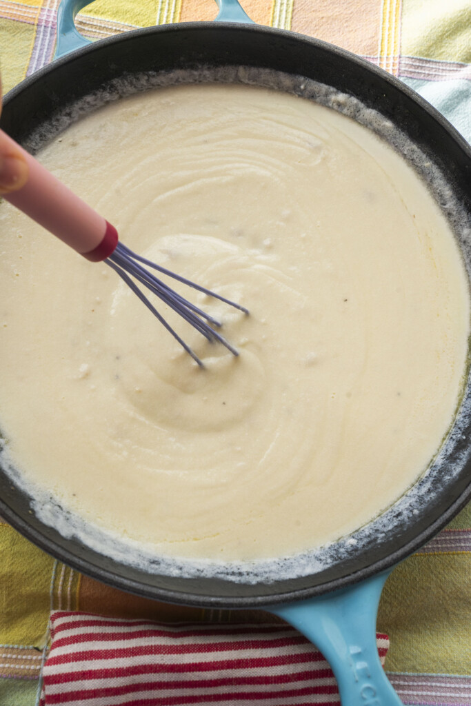 Whisking a creamy homemade Alfredo sauce in a blue skillet.