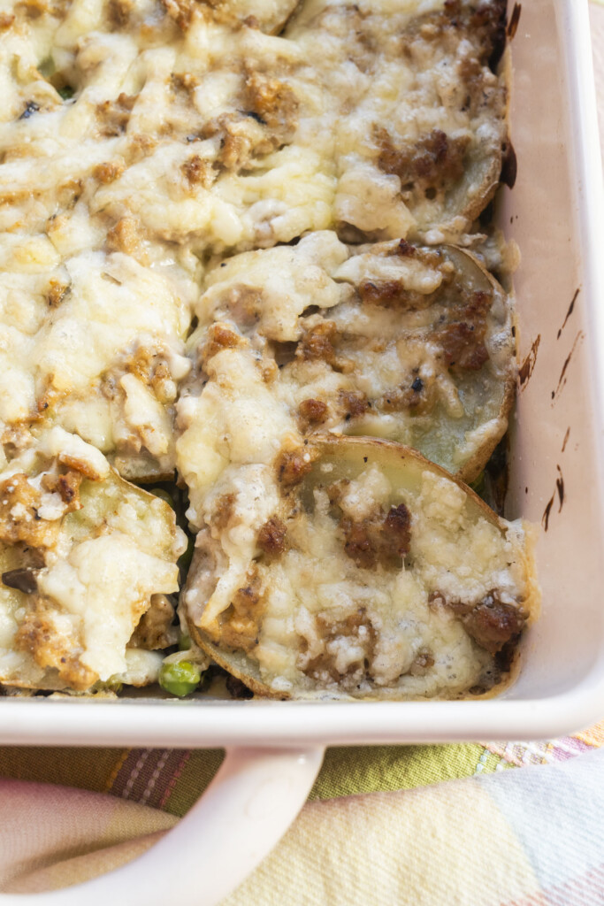A close-up view inside a white baking dish showing the golden, crispy edges of sliced potatoes and melted cheese topping a baked ground turkey casserole.