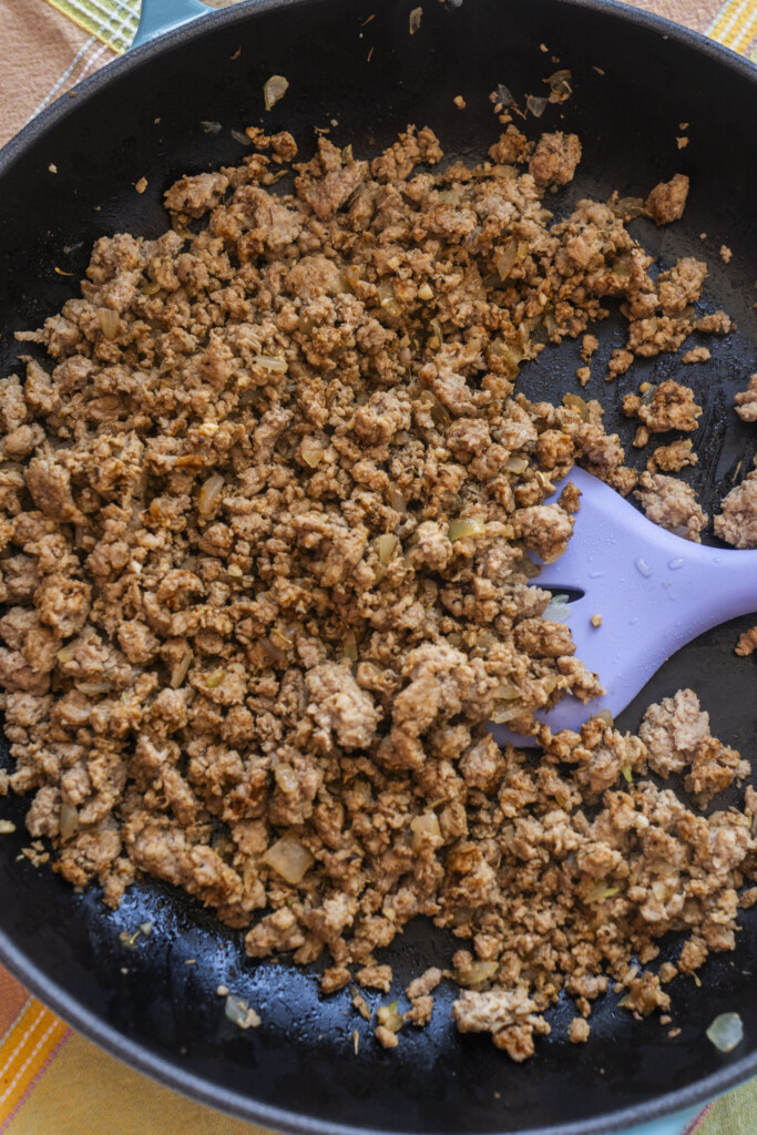 Savory ground turkey and chopped onions browned in a dark skillet with a purple spatula, preparing the hearty meat layer for an easy family dinner.