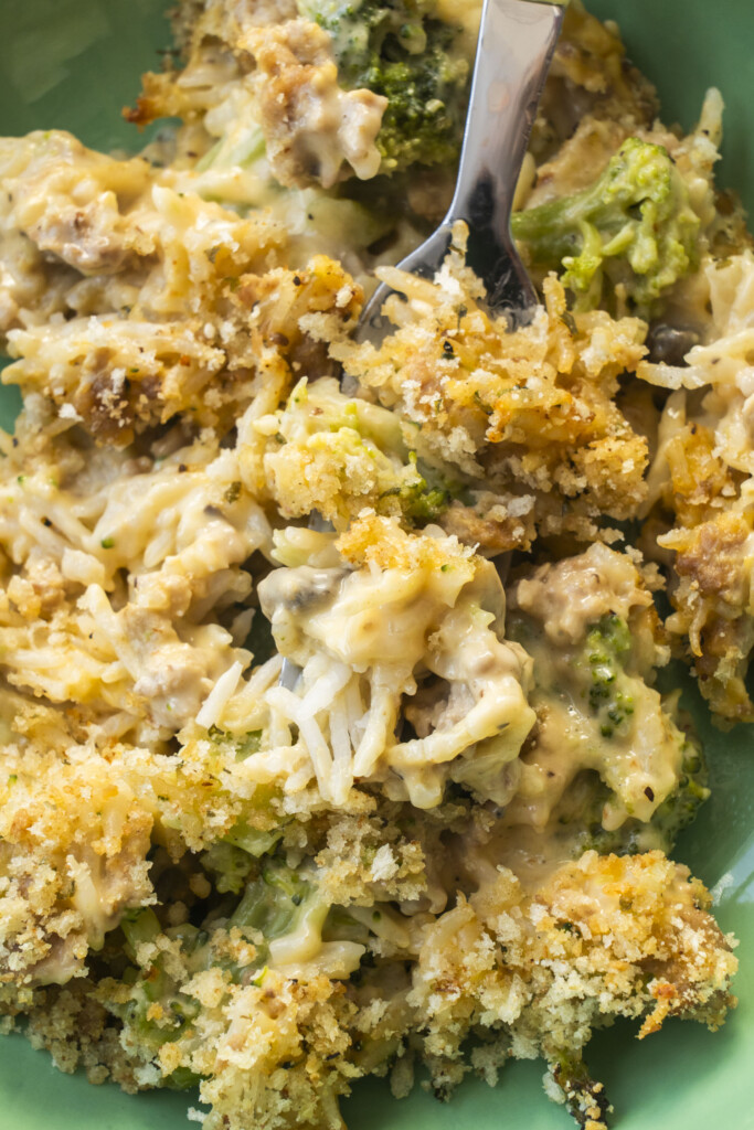 Close up of a fork digging into a serving of cheesy turkey broccoli rice casserole on a green plate.
