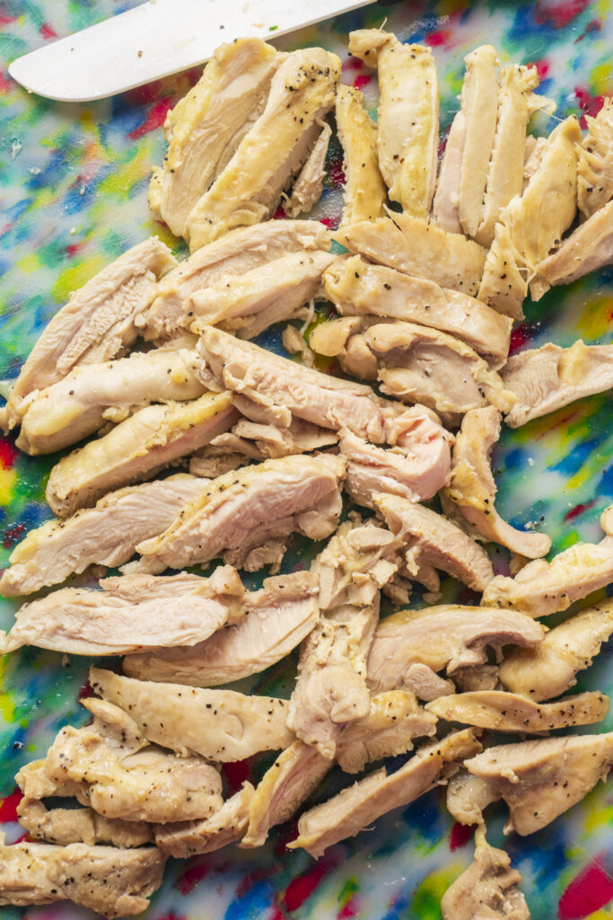 Cooked and shredded chicken thigh on colorful cutting board.
