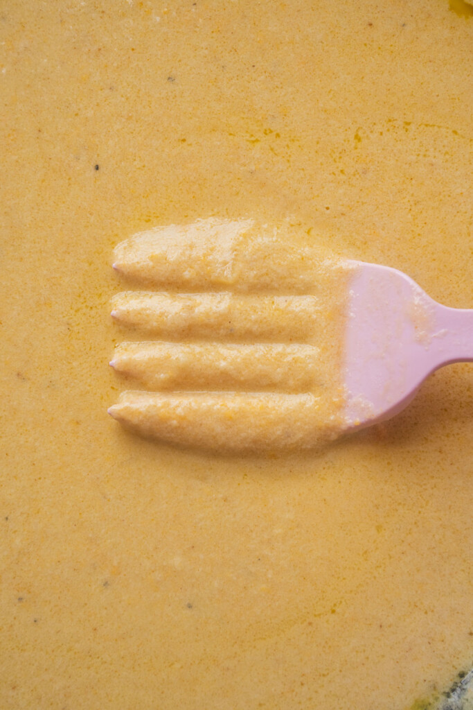 A close-up of a pink fork making grooves in a creamy orange sauce, with the fork partially covered by the sauce.