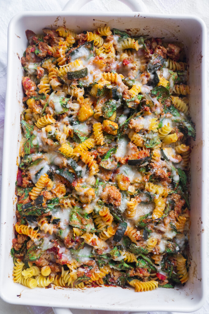 A baked pasta casserole with rotini, ground meat, spinach, tomato sauce, and melted cheese in a white rectangular dish.
