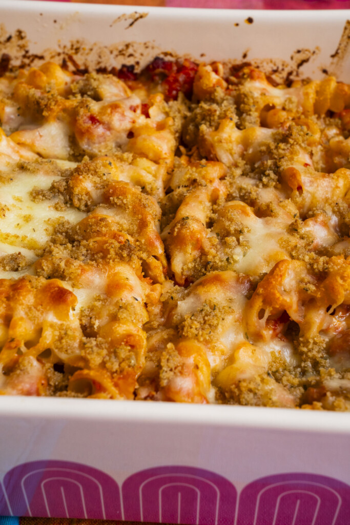 A close-up of a baked pasta casserole in a white dish, topped with melted cheese and golden brown breadcrumbs.