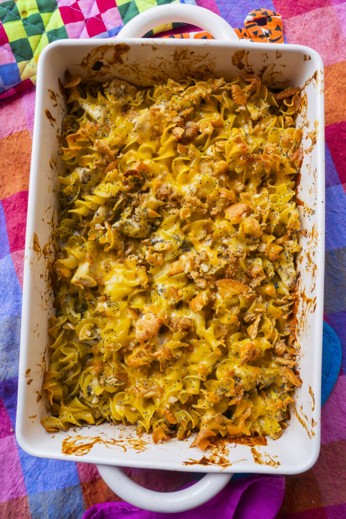 A baked casserole dish filled with cheesy egg noodles topped with a golden, crispy layer of breadcrumbs, sitting on a colorful, checkered tablecloth.