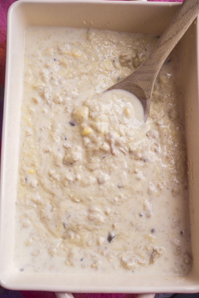 A rectangular dish filled with a creamy, chunky mixture being stirred with a wooden spoon.