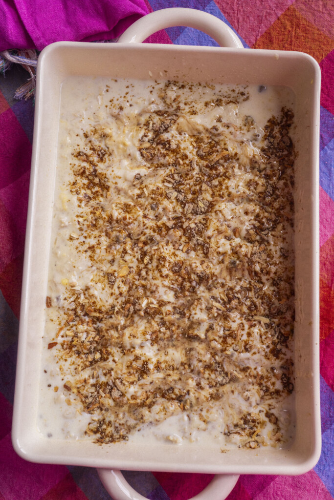 A rectangular baking dish filled with a creamy mixture topped with a sprinkling of onion soup mix, resting on a pink and orange checkered cloth.