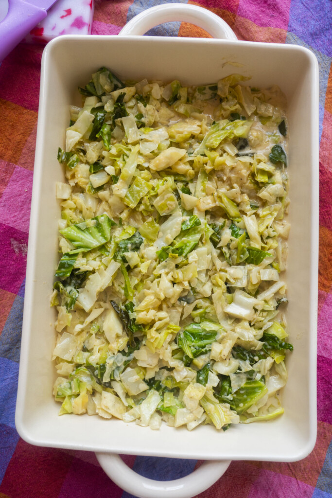 A rectangular white baking dish filled with a creamy chopped cabbage casserole, set on a colorful, checkered cloth.