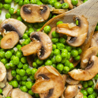Sautéed mushrooms and green peas mixed together, with a wooden spoon stirring the vegetables. The mushrooms are sliced and lightly browned, while the peas appear bright and fresh.
