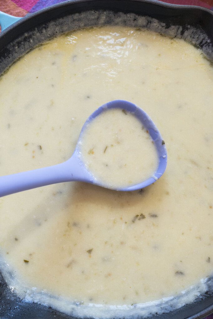 A blue ladle lifts a creamy queso sauce.