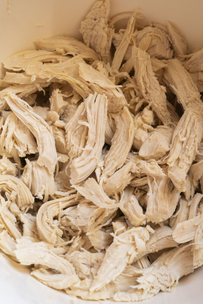 Shredded, cooked chicken breast pieces piled together in a white bowl, showing moist and fibrous texture.