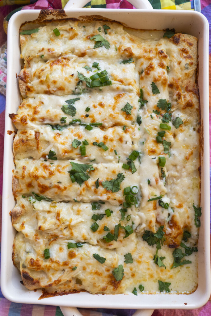 A baking dish filled with cheesy enchiladas, topped with melted cheese, chopped green onions, and cilantro, ready to be served.